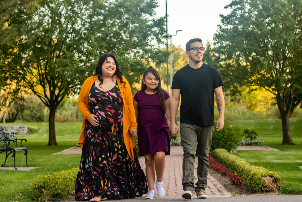 Family of 3 walking towards the camera on a brick path with the mom holding her pregnant belly at the International Peace Gardens in Salt Lake